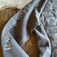 Gray quilted jacket with 'Ranch Girls' embroidery on a wooden surface.