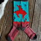 A pair of knee-high socks laid flat on a rustic wooden surface. The socks feature a turquoise upper section with a red cowboy riding a bucking horse, dark gray cuffs and heels, and a dark red lower section with textured knit patterns.