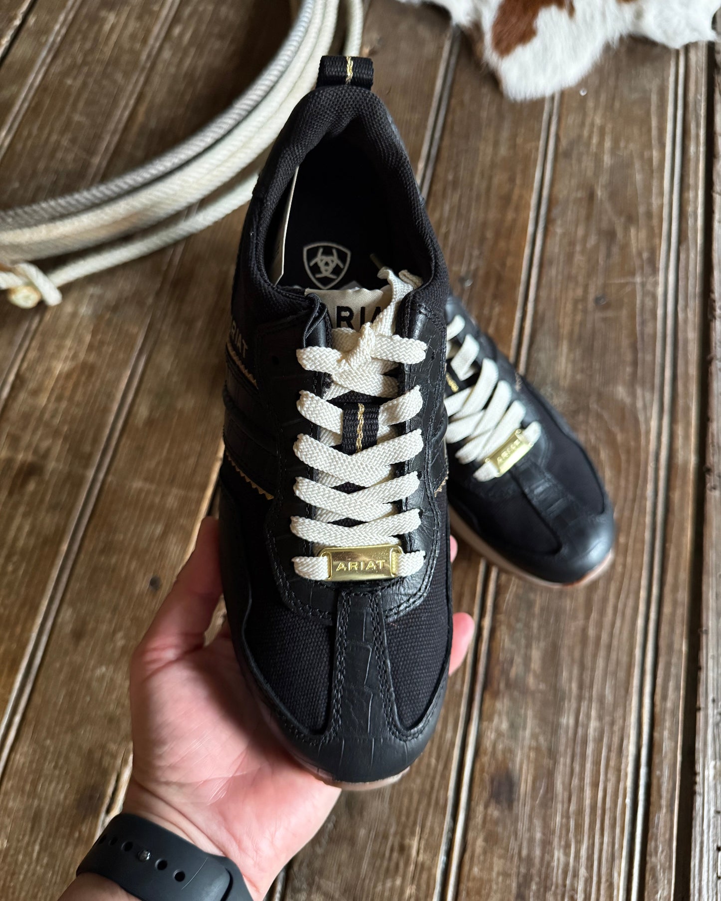 Black sneakers with white laces held by a hand on a wooden surface