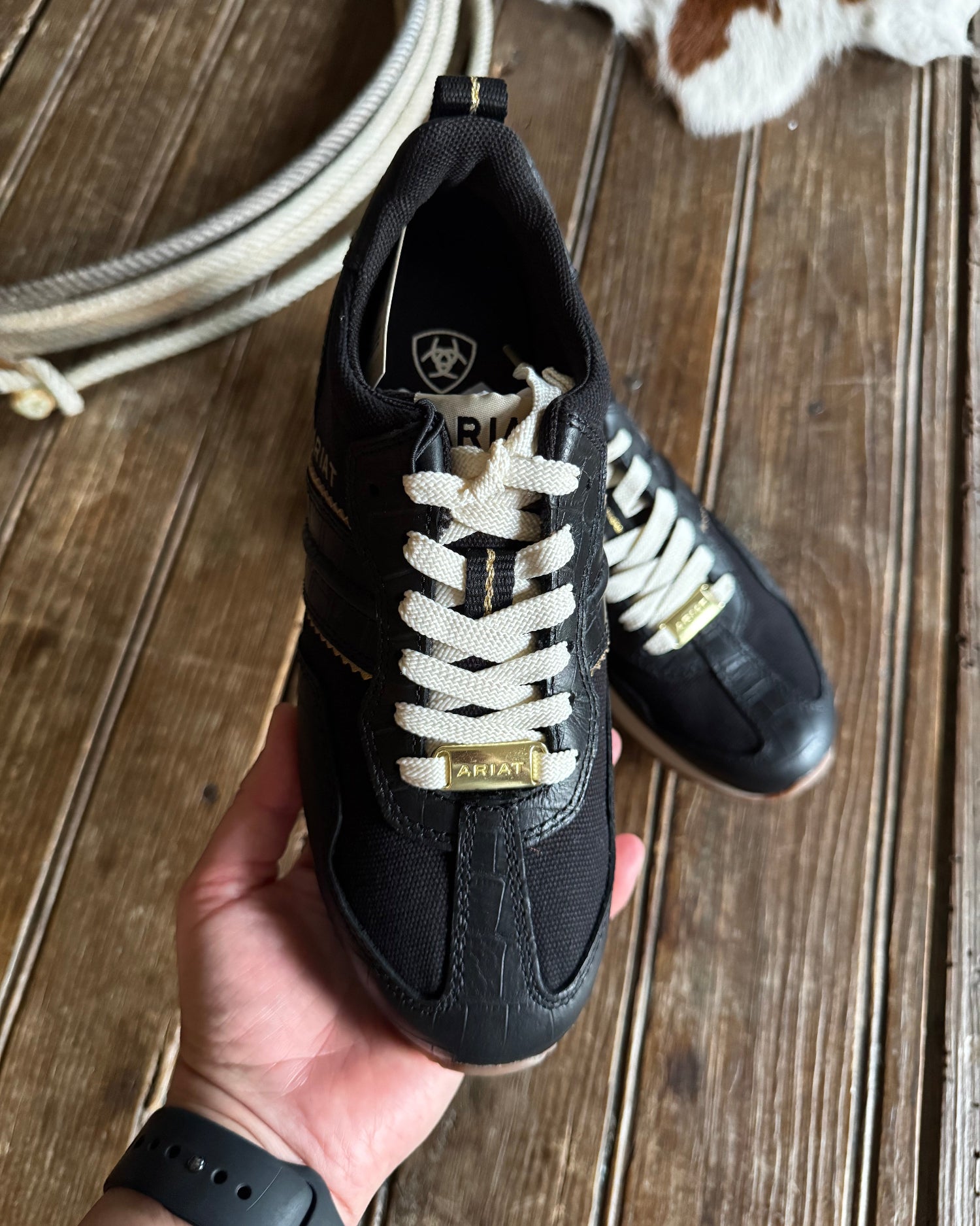 Black sneakers with white laces held by a hand on a wooden surface