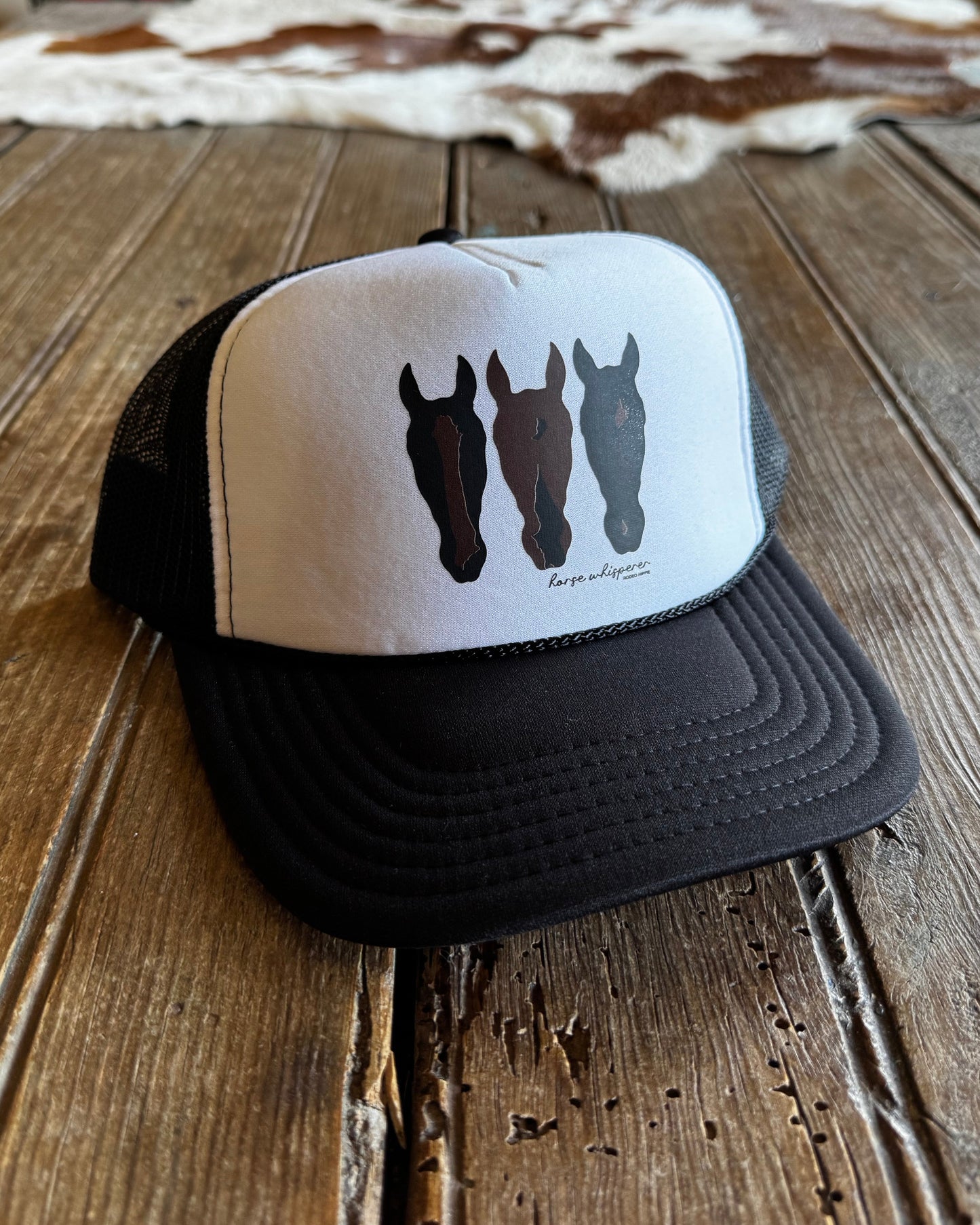 Black and white cap with horse designs on a wooden surface