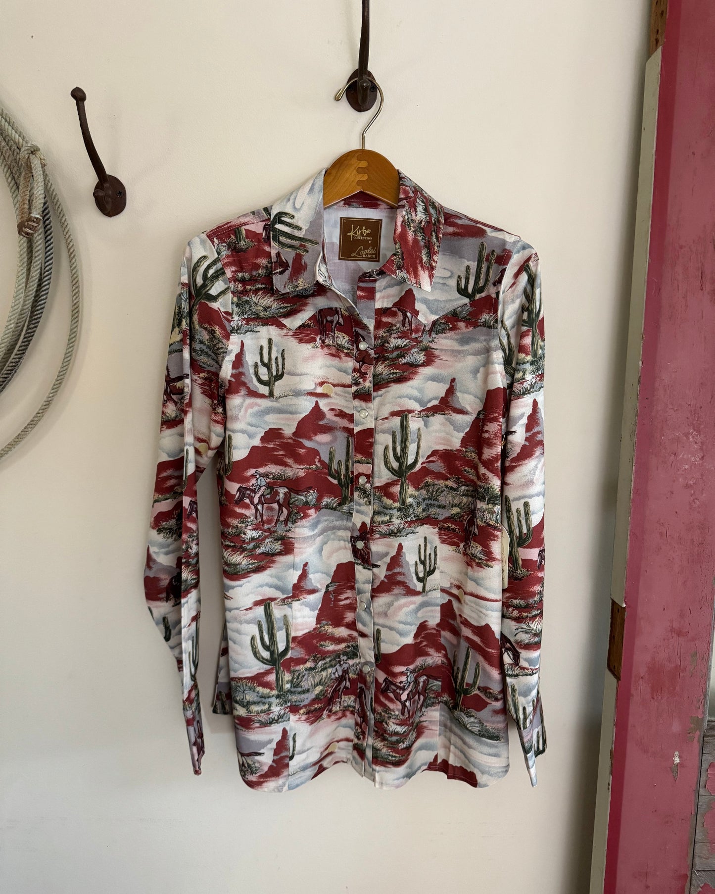Long-sleeve shirt with cactus pattern hanging on a hook against a white wall.