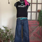Mannequin wearing a black sleeveless top with 'HOWDY' text, blue jeans, and a pink scarf in a room setting.