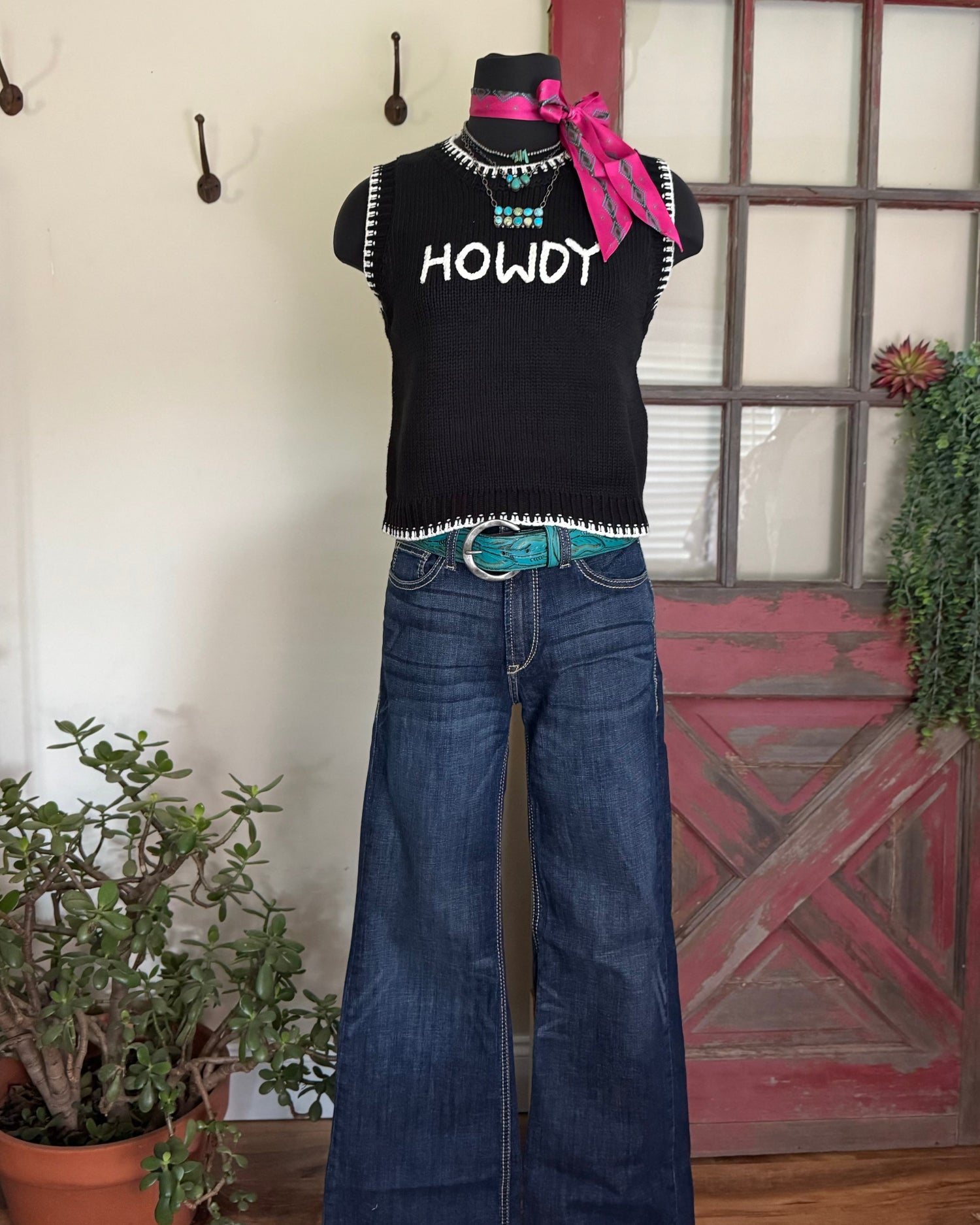 Mannequin wearing a black sleeveless top with 'HOWDY' text, blue jeans, and a pink scarf in a room setting.