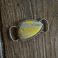 Silver twilly slide with a yellow stone on a wooden surface