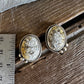 A pair of oval stud earrings with textured cream and gold-toned stone centers in silver-toned bezel settings, displayed on a rustic wooden surface next to a metal ruler for scale.