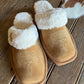 Pair of tan slippers with white fur lining on a wooden floor.