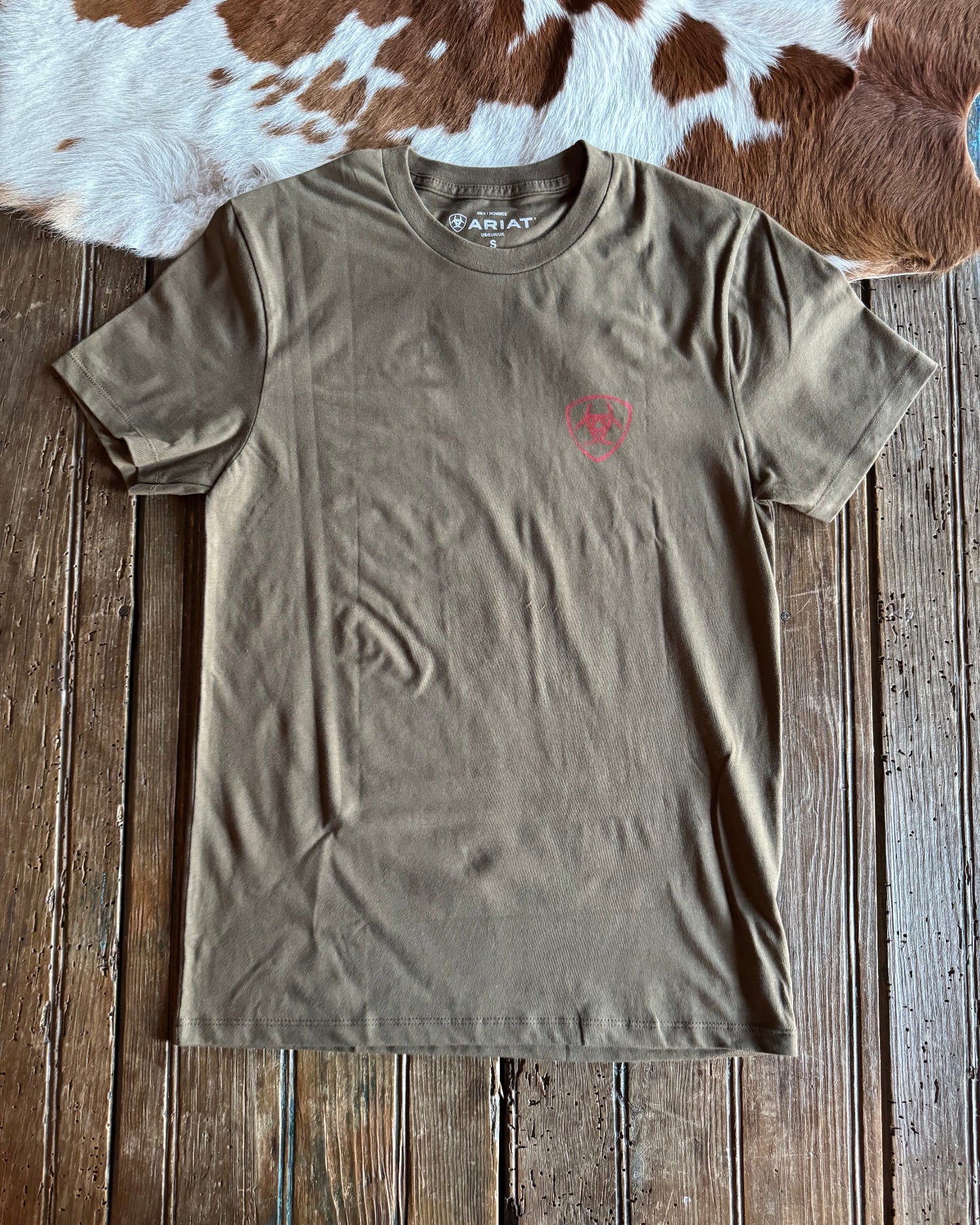 Green t-shirt with a red logo on a wooden surface next to a cowhide rug