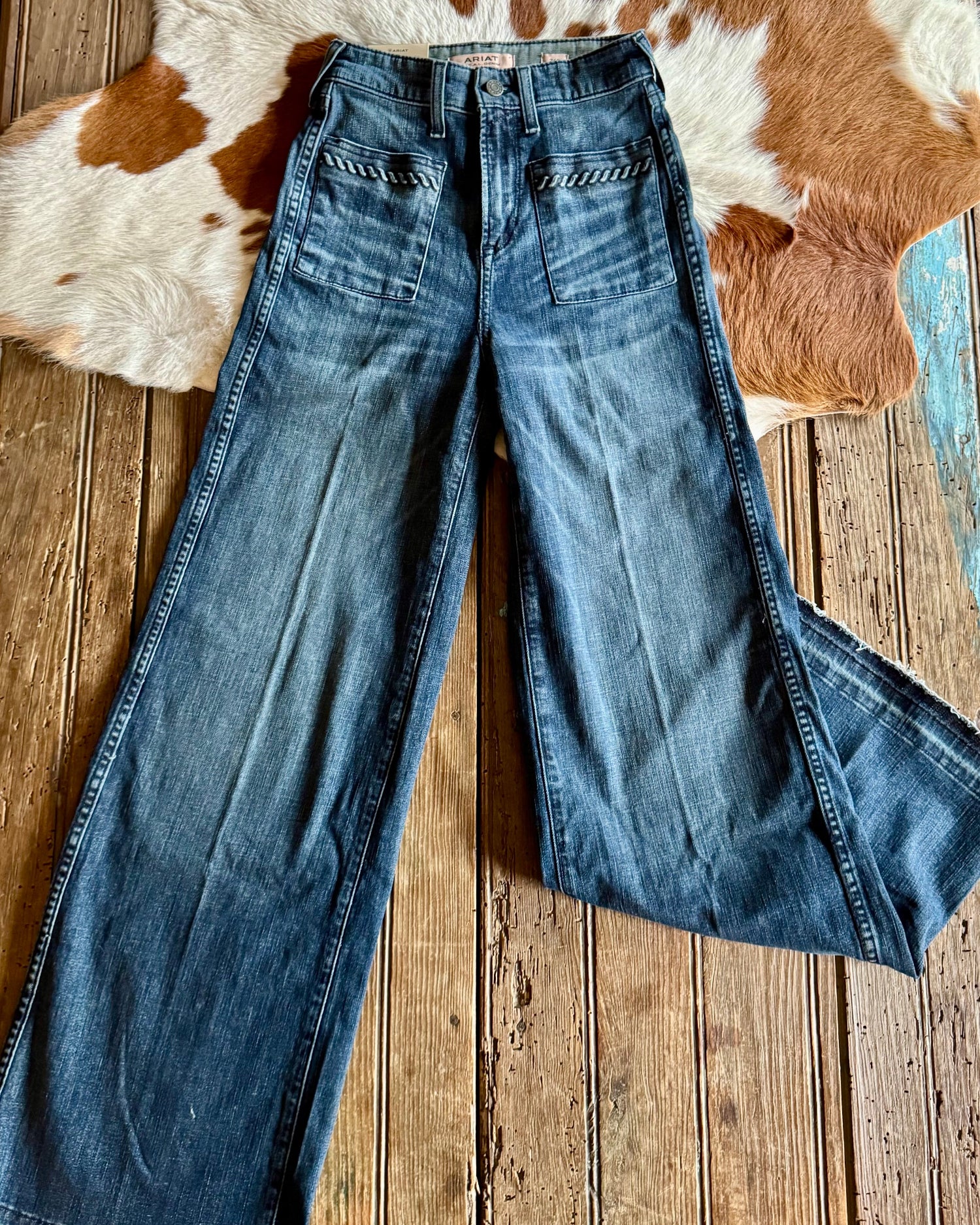 Blue jeans laid flat on a wooden surface with a cowhide rug in the background