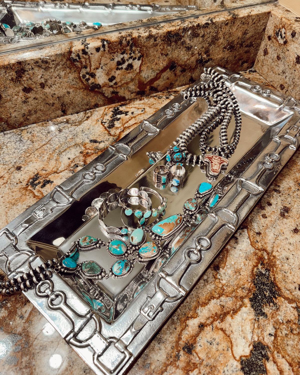 Silver and turquoise jewelry set on a decorative tray with a textured surface