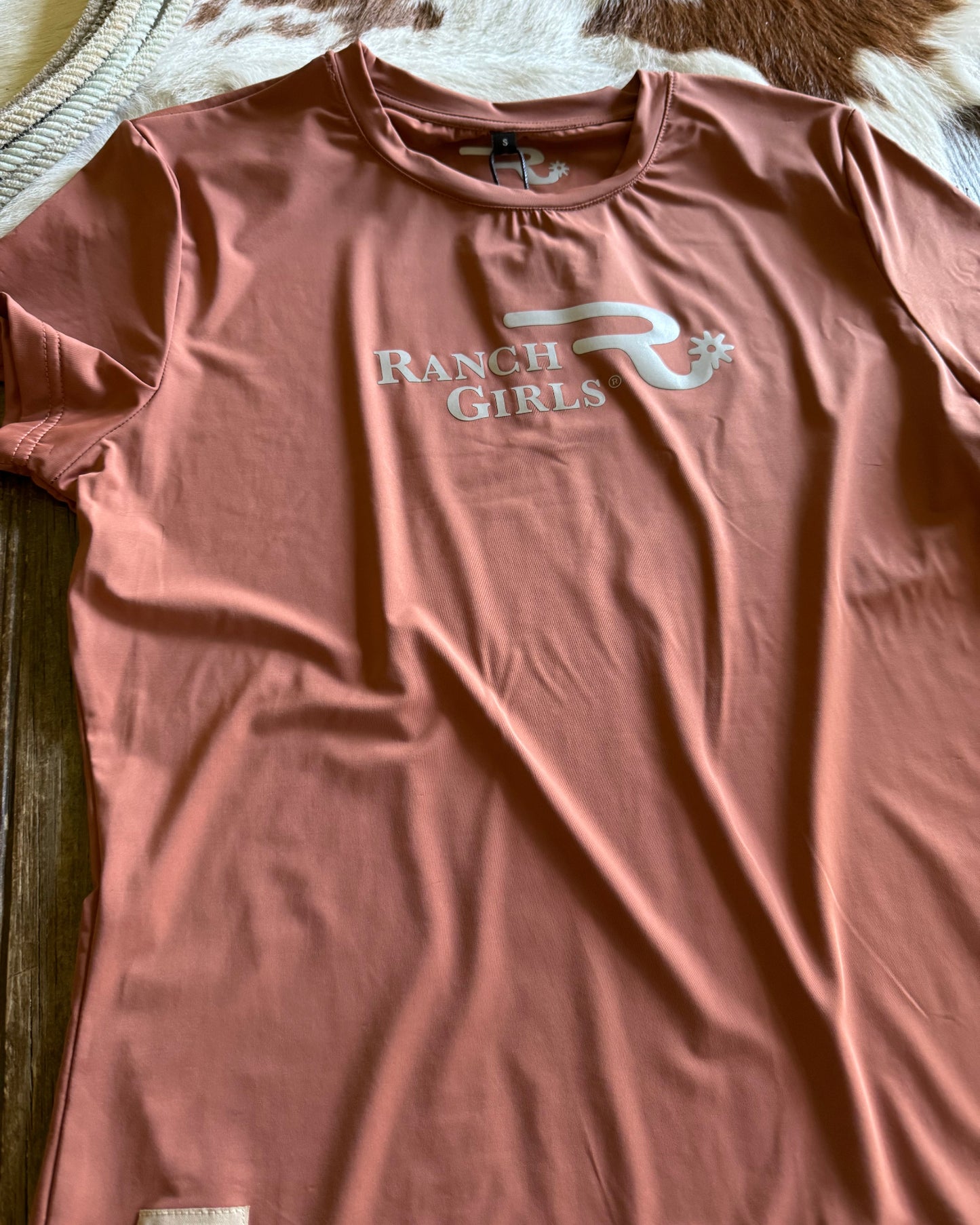 Pink t-shirt with 'Ranch Girls' logo on a textured surface