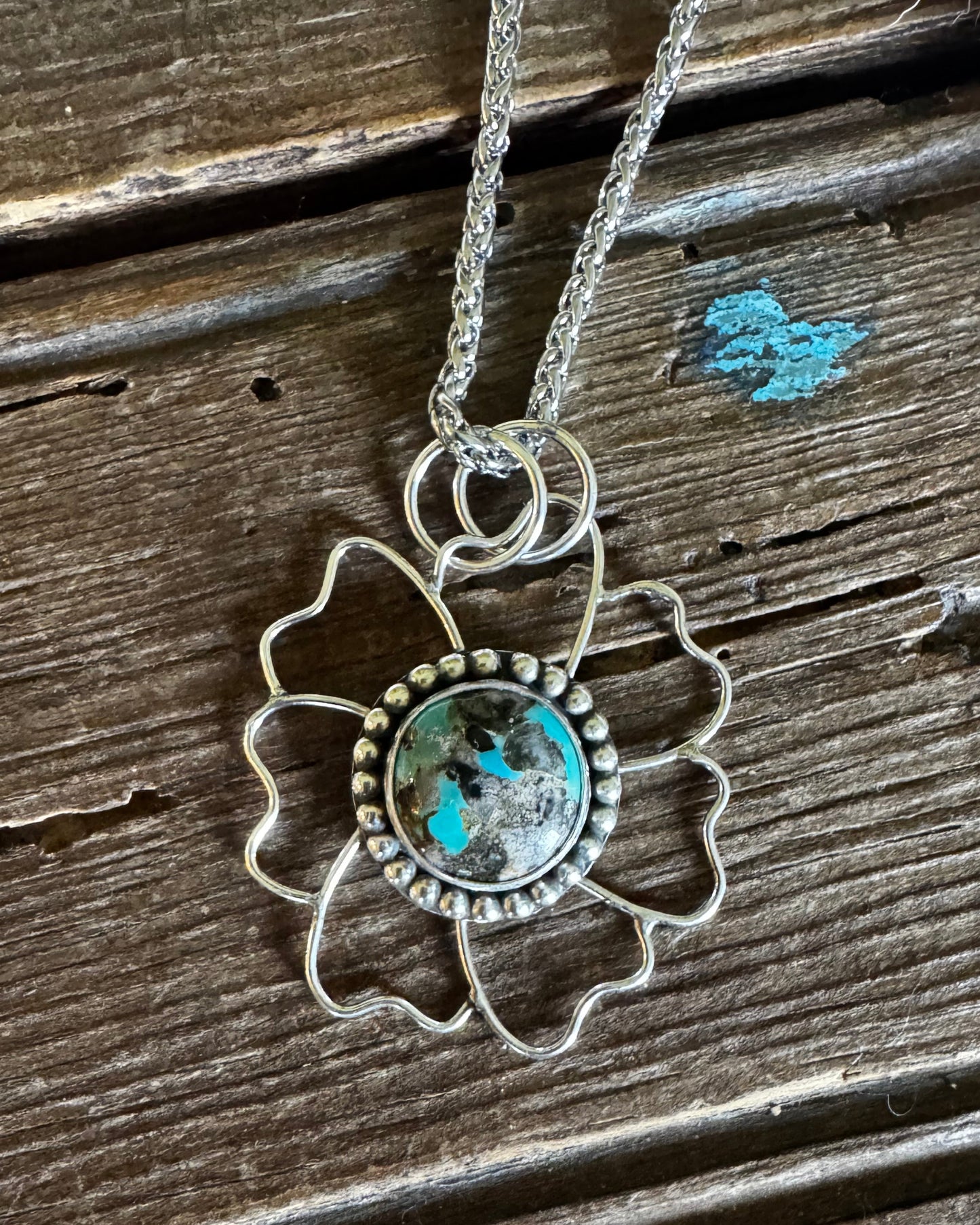 Necklace with a floral pendant featuring turquoise stone on a wooden surface