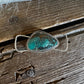 A Southwestern-style sterling silver ring featuring a large, irregular turquoise stone with natural brown and black matrix inclusions, resting on a rustic weathered wooden surface.