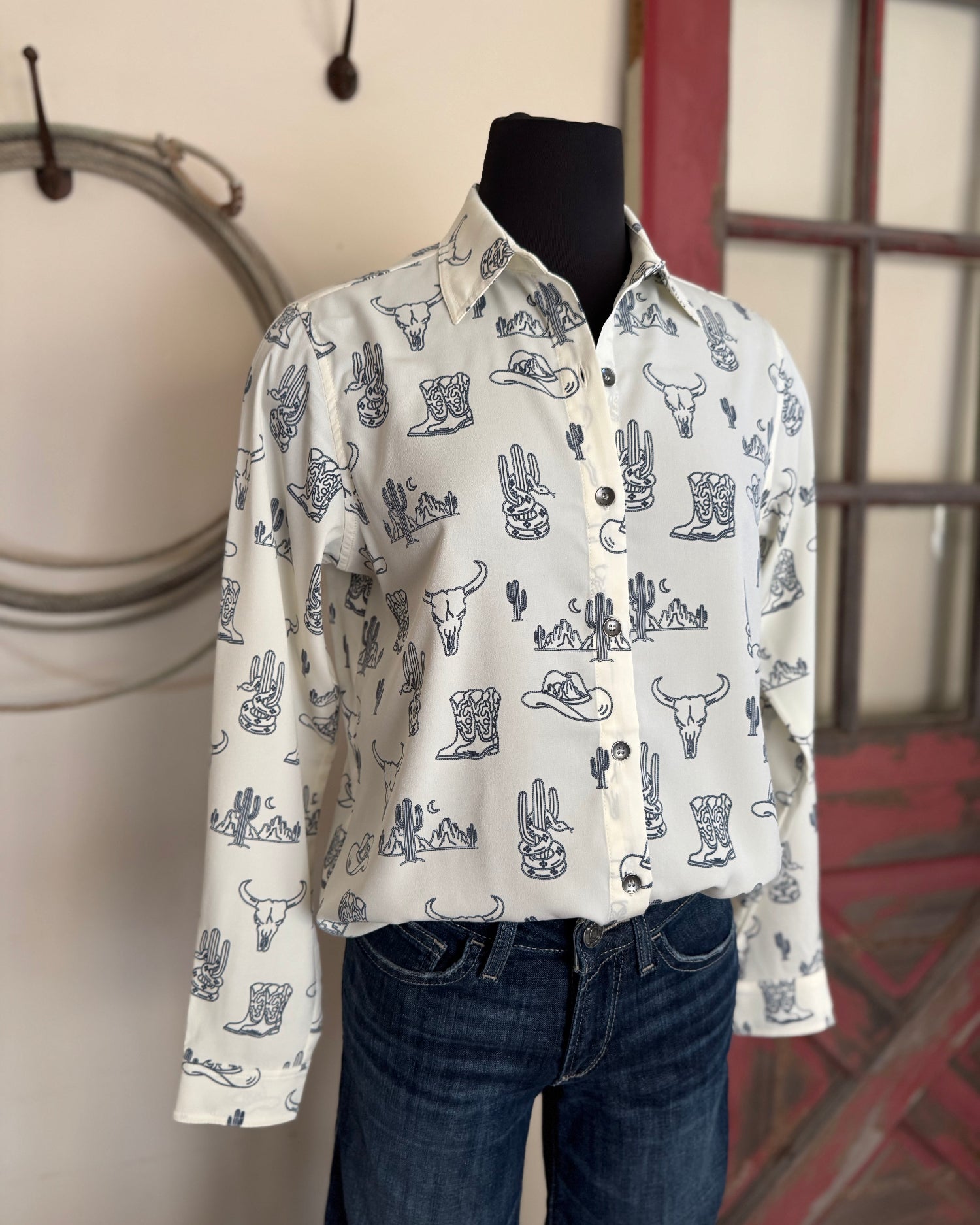 Mannequin wearing a white shirt with blue patterns in a room with a window and wall decor.