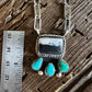Silver and turquoise jewelry piece on a wooden surface with a ruler for scale.