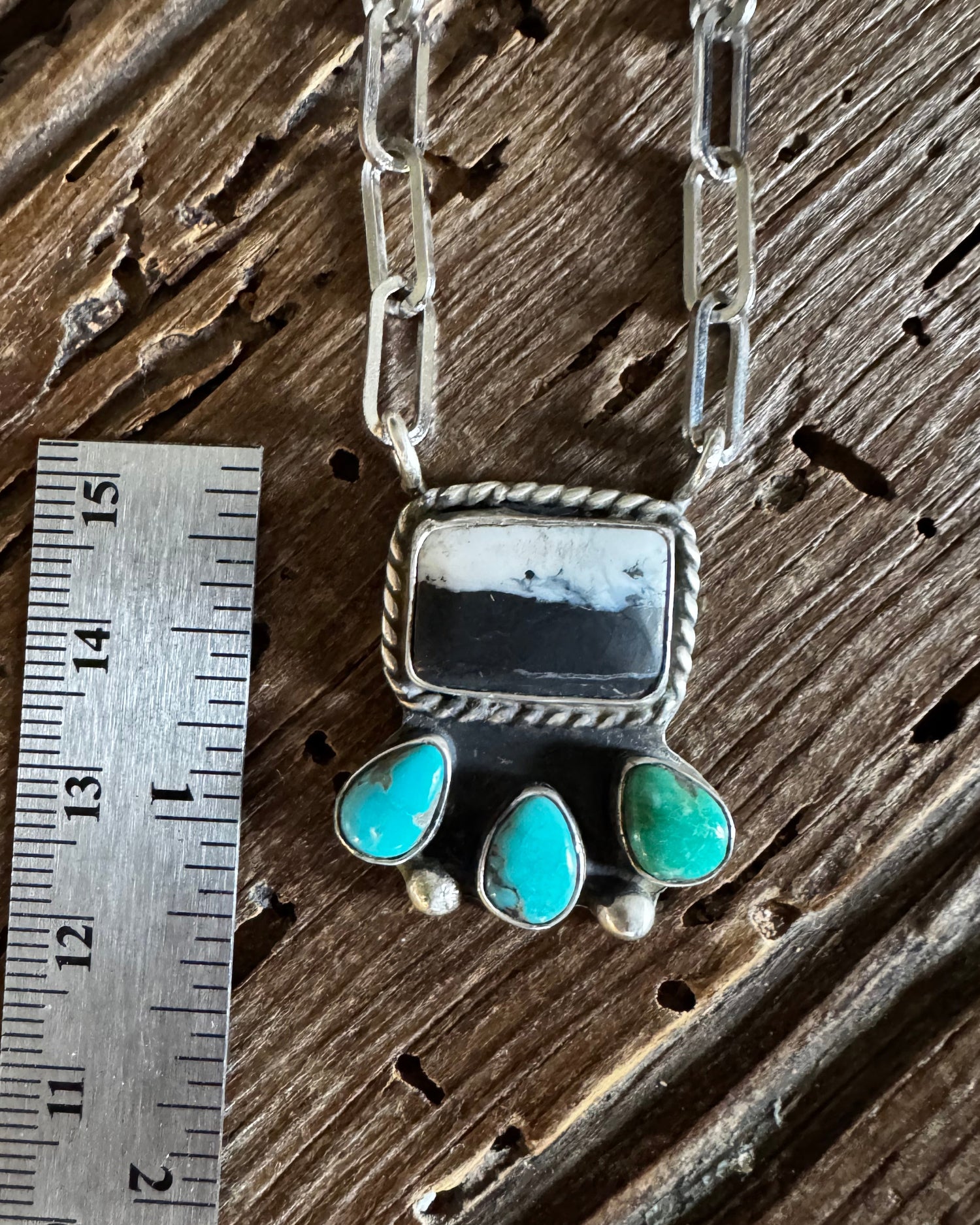 Silver and turquoise jewelry piece on a wooden surface with a ruler for scale.