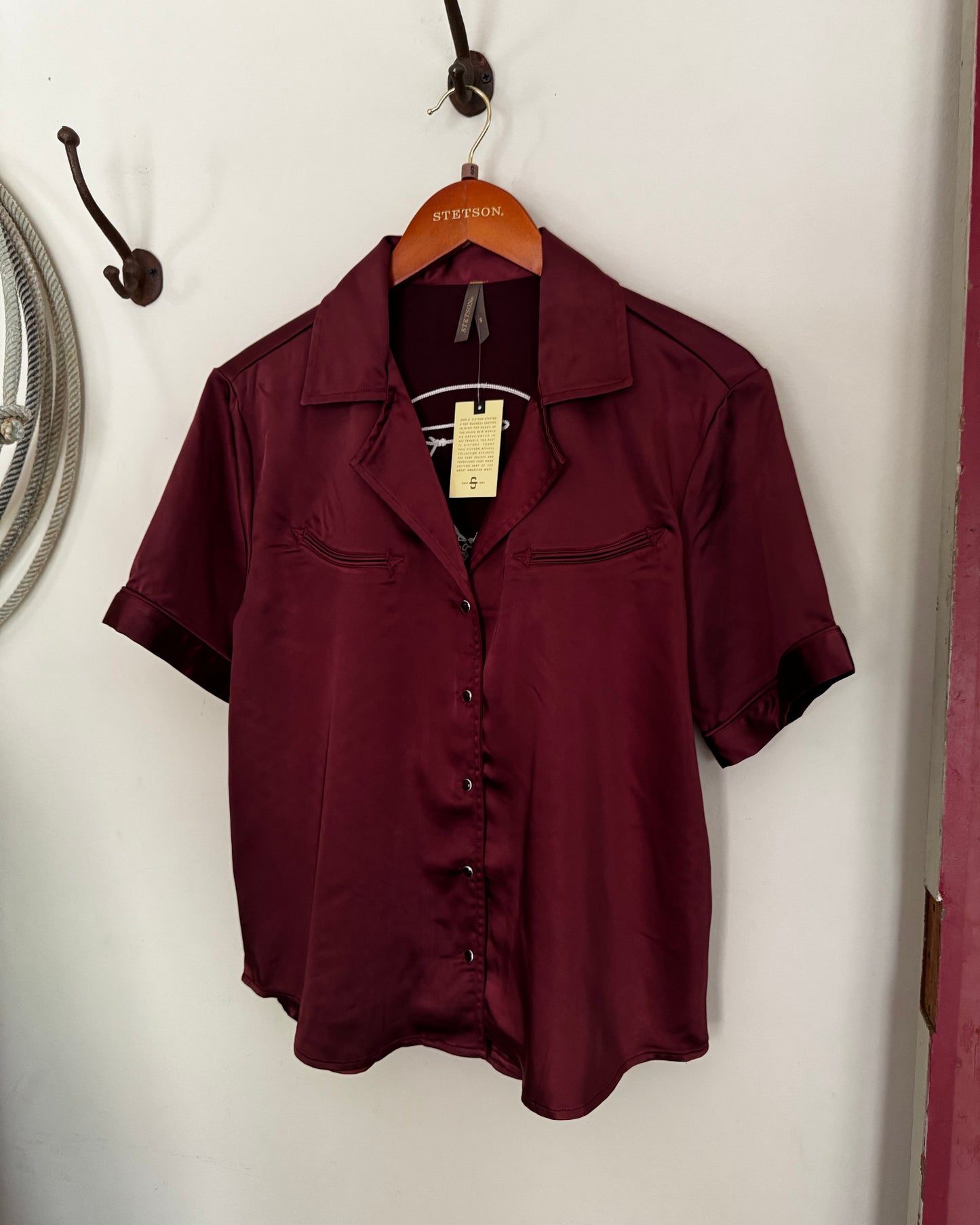 Maroon shirt on a hanger with a tag against a white background