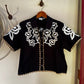 Floral embroidered blouse hanging on a white wall.