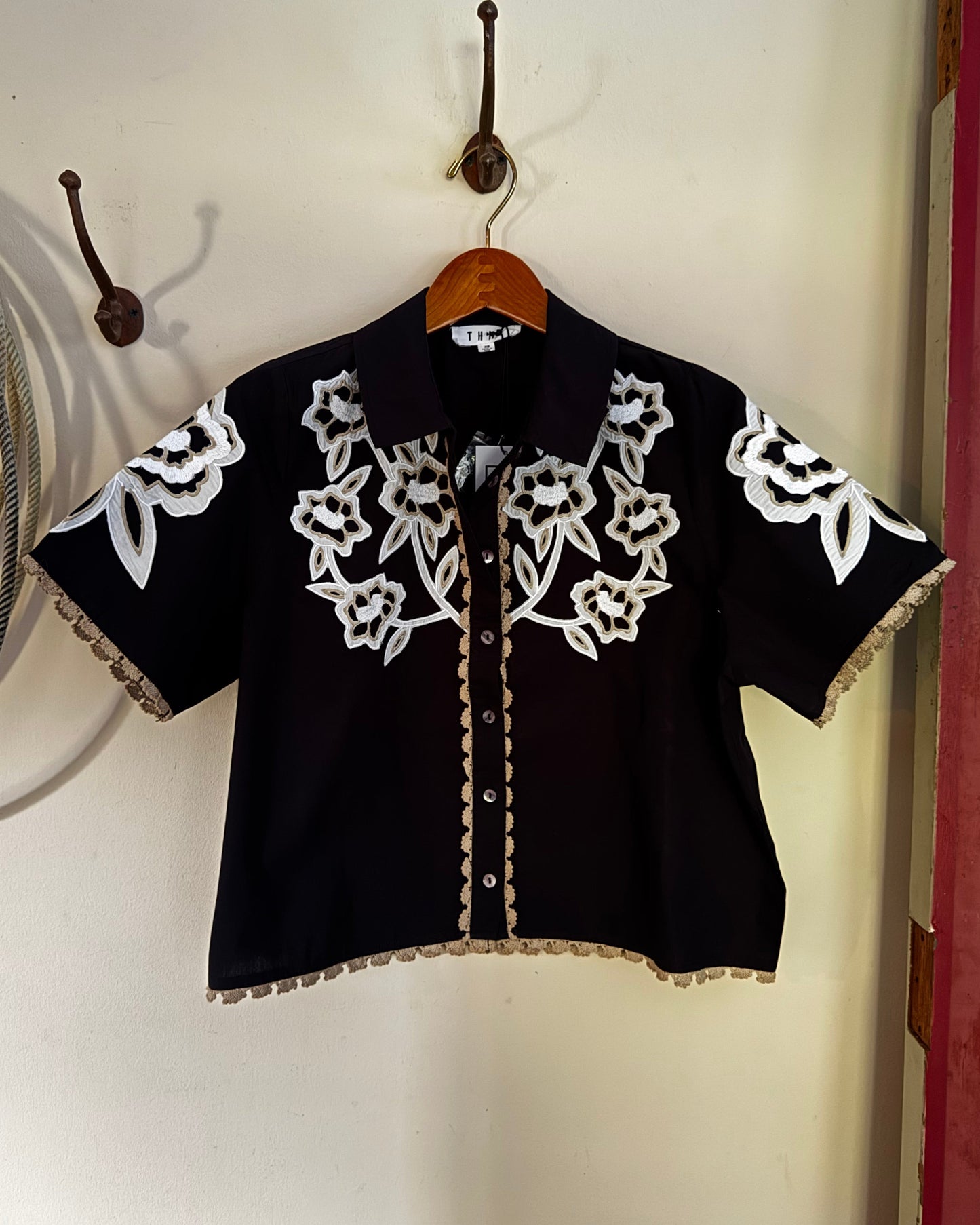 Floral embroidered blouse hanging on a white wall.