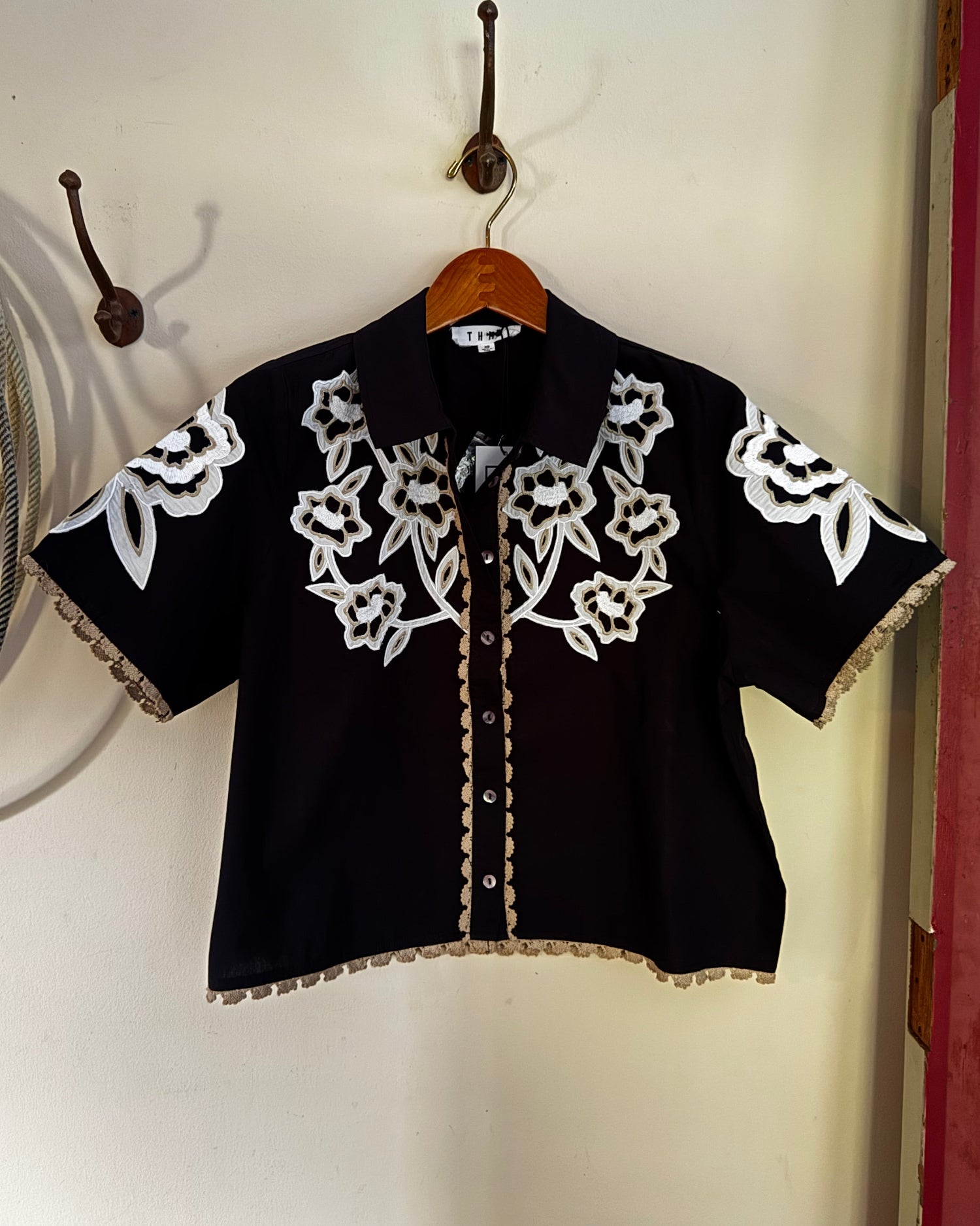 Floral embroidered blouse hanging on a white wall.