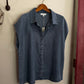 Blue denim shirt on a wooden hanger against a white wall.