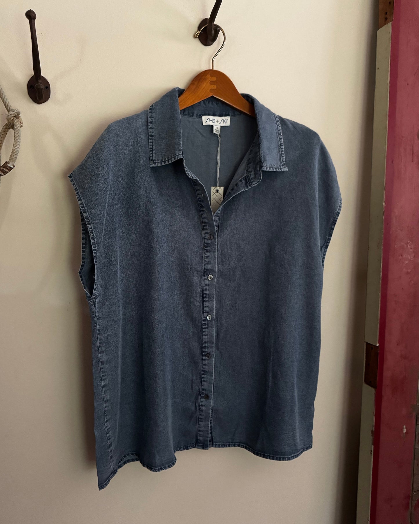 Blue denim shirt on a wooden hanger against a white wall.