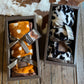 Two cowhide patterned blankets in wooden boxes on a wooden surface.