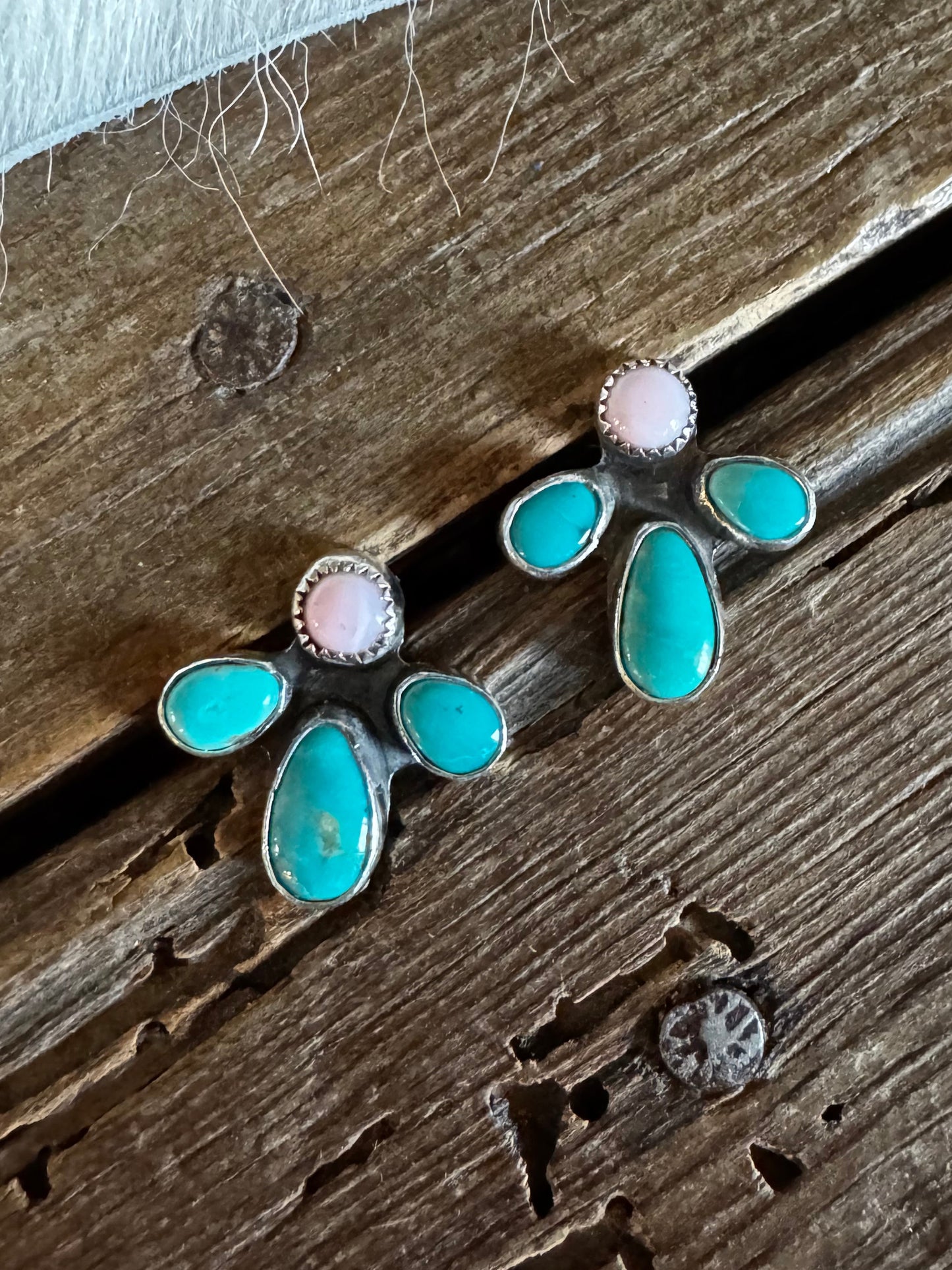 A pair of silver stud earrings with turquoise and pink stones, displayed on a rustic wooden surface.