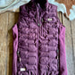 Purple quilted vest on a wooden surface with a cowhide rug in the background