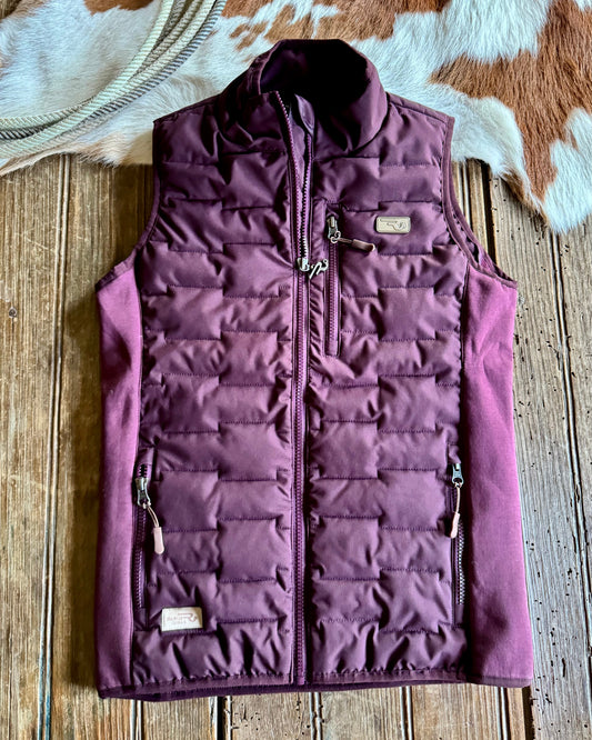 Purple quilted vest on a wooden surface with a cowhide rug in the background