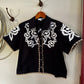 Embroidered black floral blouse hanging on a wall next to a rope
