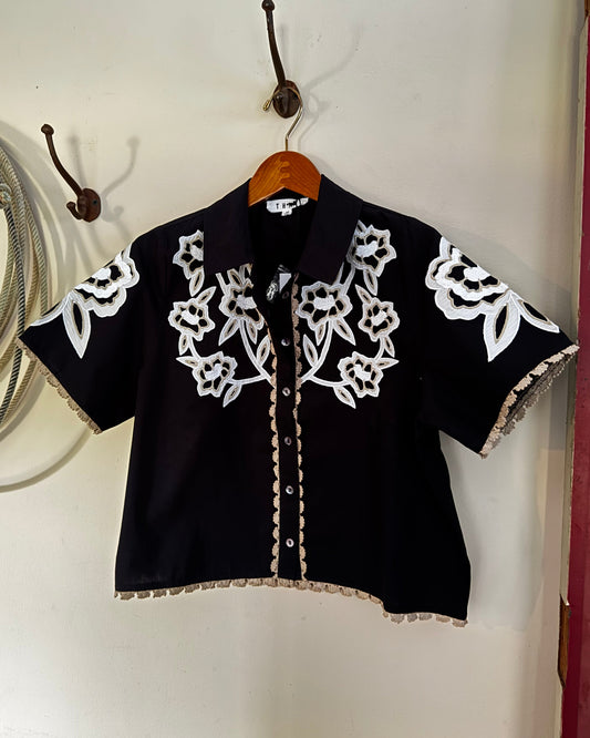 Embroidered black floral blouse hanging on a wall next to a rope