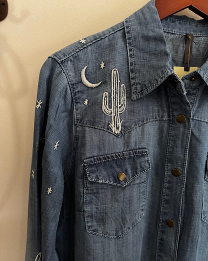 Blue denim jacket with cactus and moon designs on a beige background