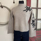 Gray sweater with black floral embroidery on a mannequin against a neutral wall.