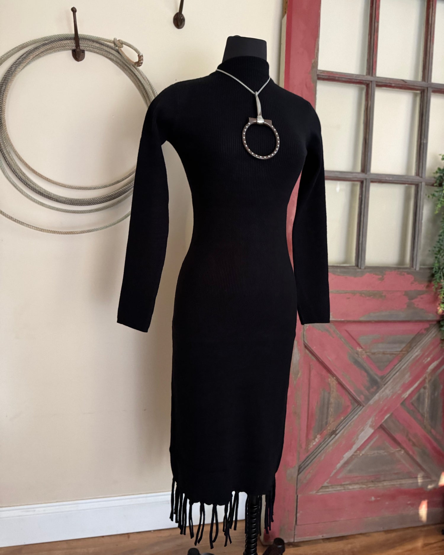 Black dress with fringe on a mannequin against a rustic background