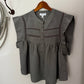 Green blouse with lace details on a wooden hanger against a white wall.