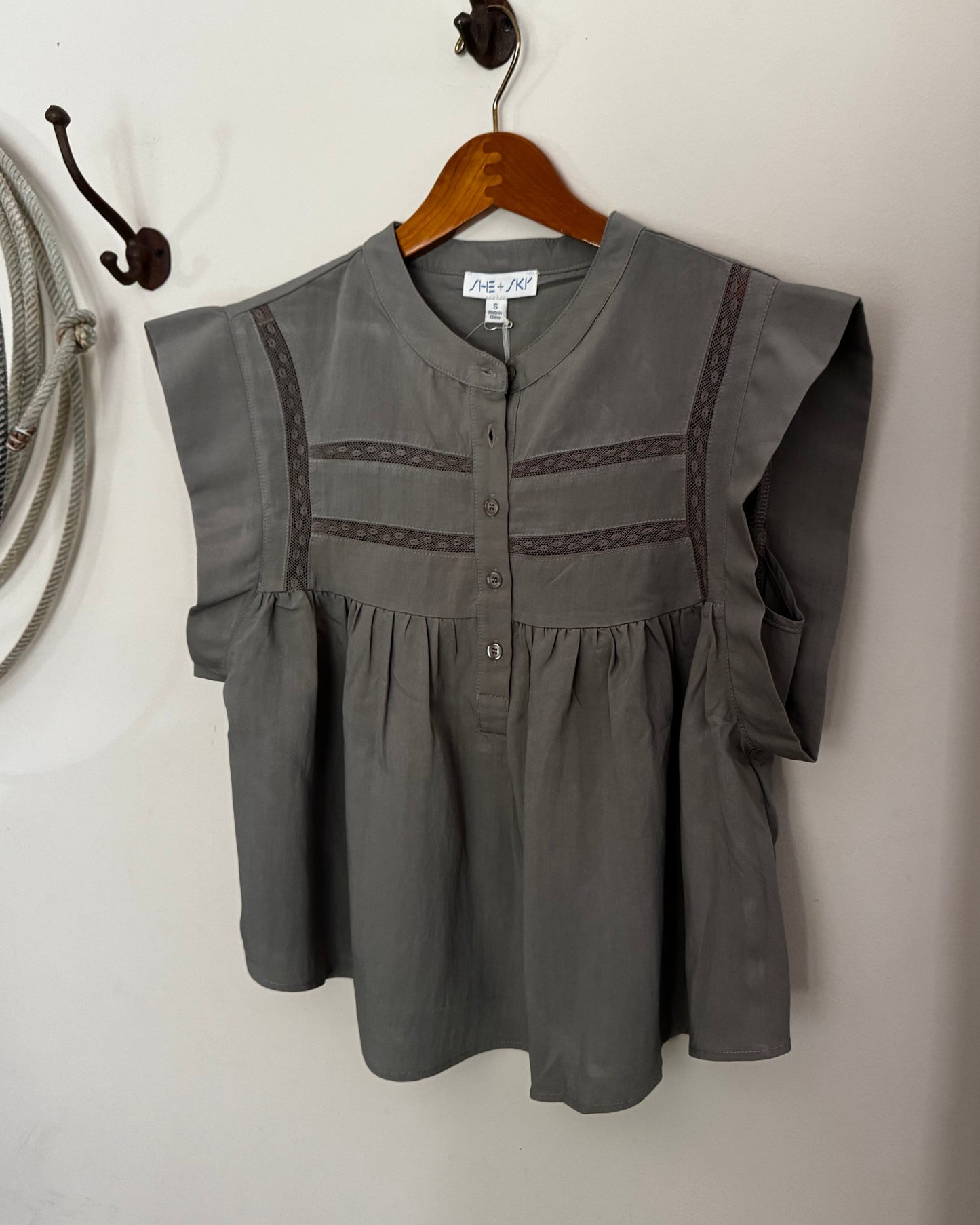 Green blouse with lace details on a wooden hanger against a white wall.
