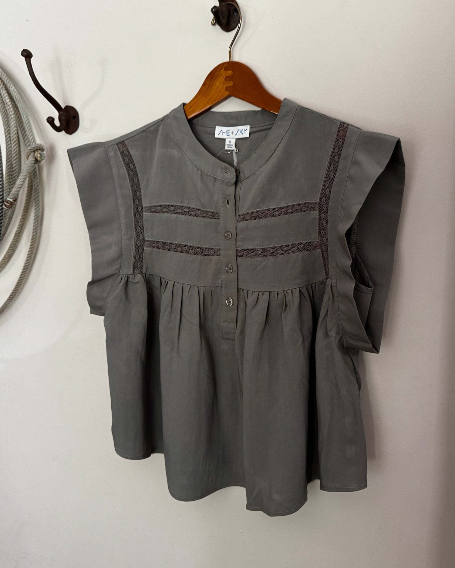 Green blouse with lace details on a wooden hanger against a white wall.