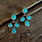 A pair of silver-toned dangle earrings with turquoise blue stones, resting on a rustic dark brown wooden surface.