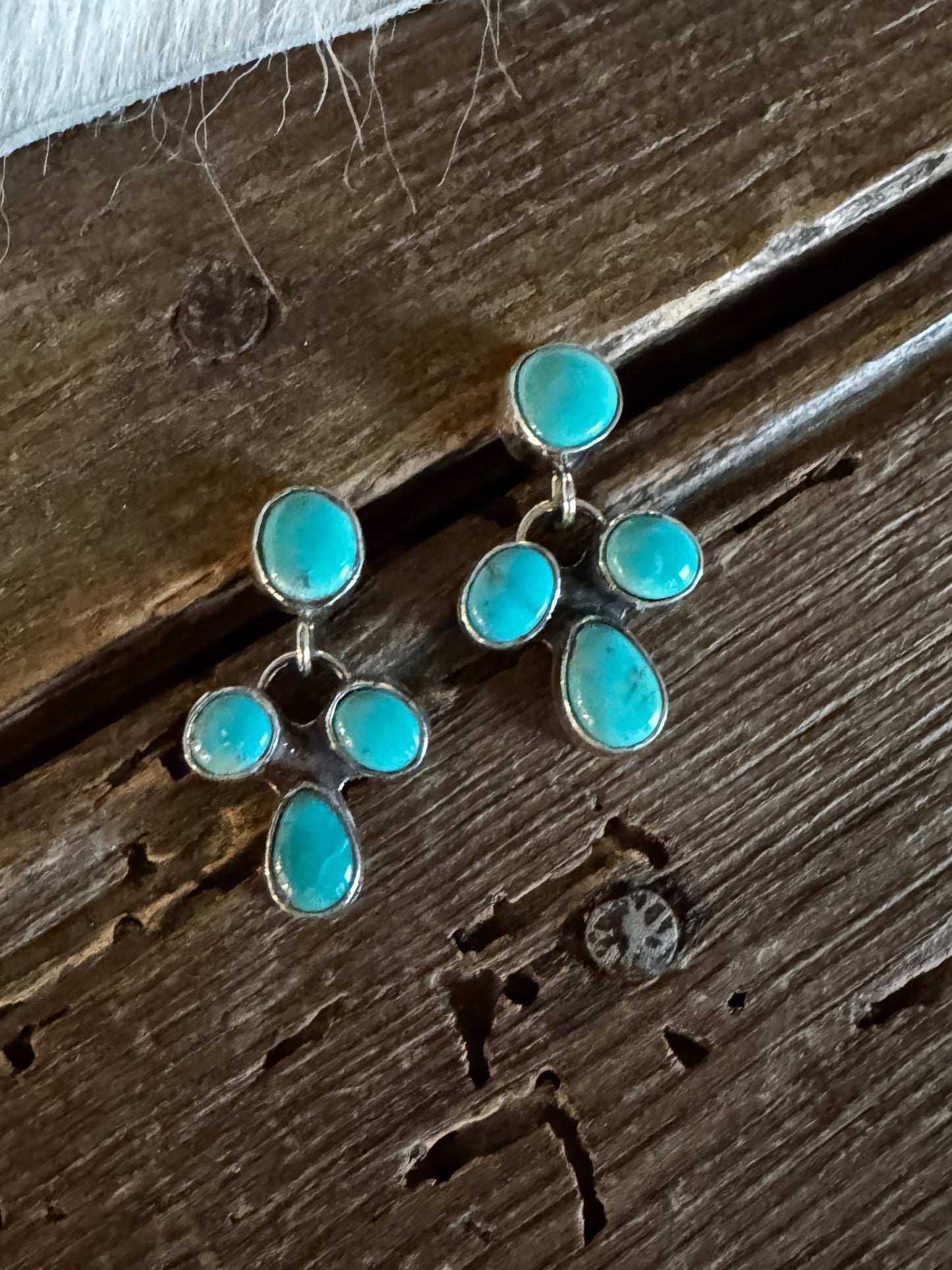 A pair of silver-toned dangle earrings with turquoise blue stones, resting on a rustic dark brown wooden surface.