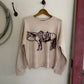 Beige sweater with a brown graphic design on a wooden hanger against a white wall.