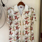 A short-sleeve button-up shirt with a white base and a colorful cowboy print, hanging on a wooden hanger against a plain wall.