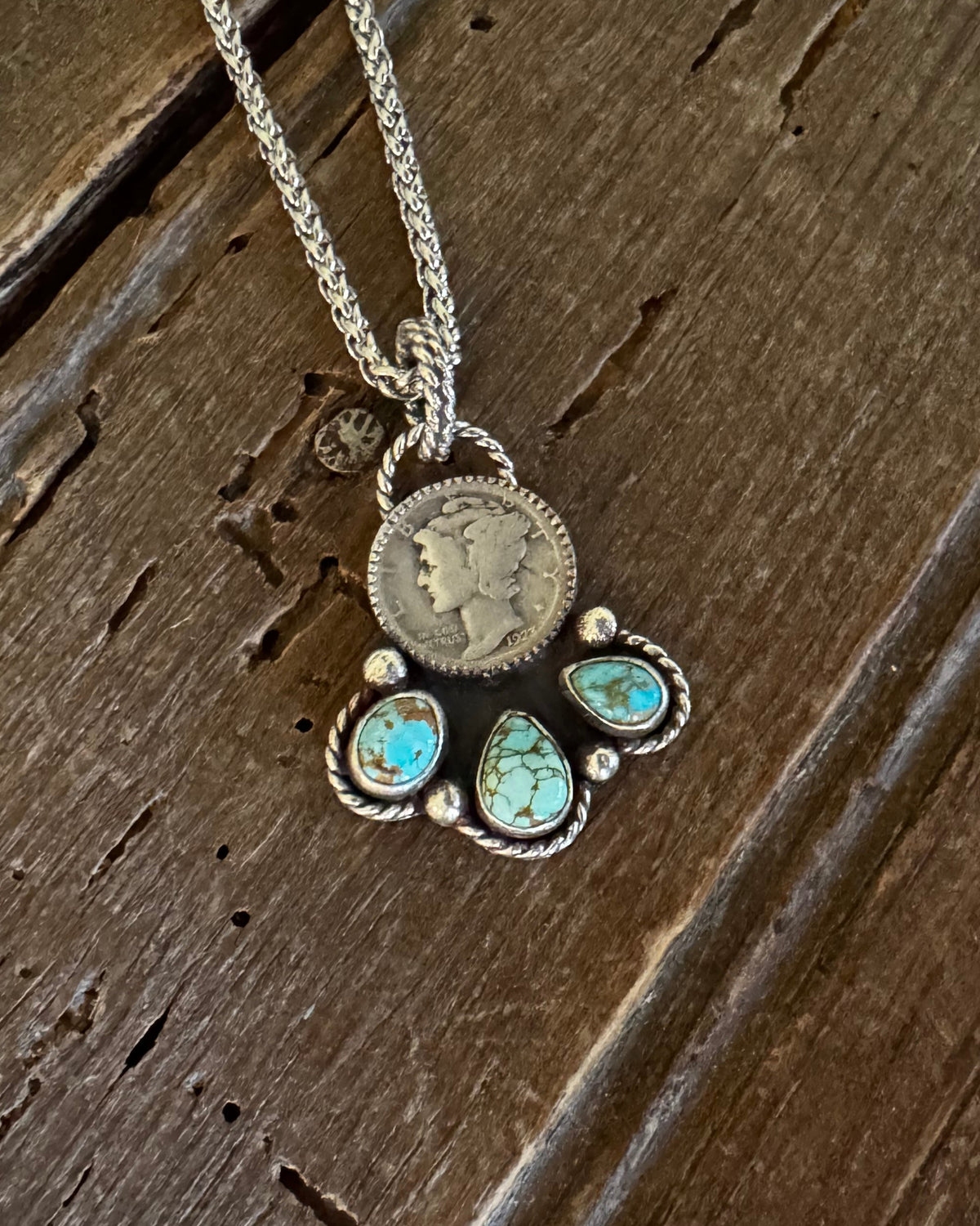 Liberty dime pendant with turquoise stones on a wooden background