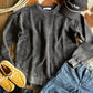 Gray sweatshirt, yellow moccasins, blue jeans, and a black cap on a wooden surface with a cowhide rug.