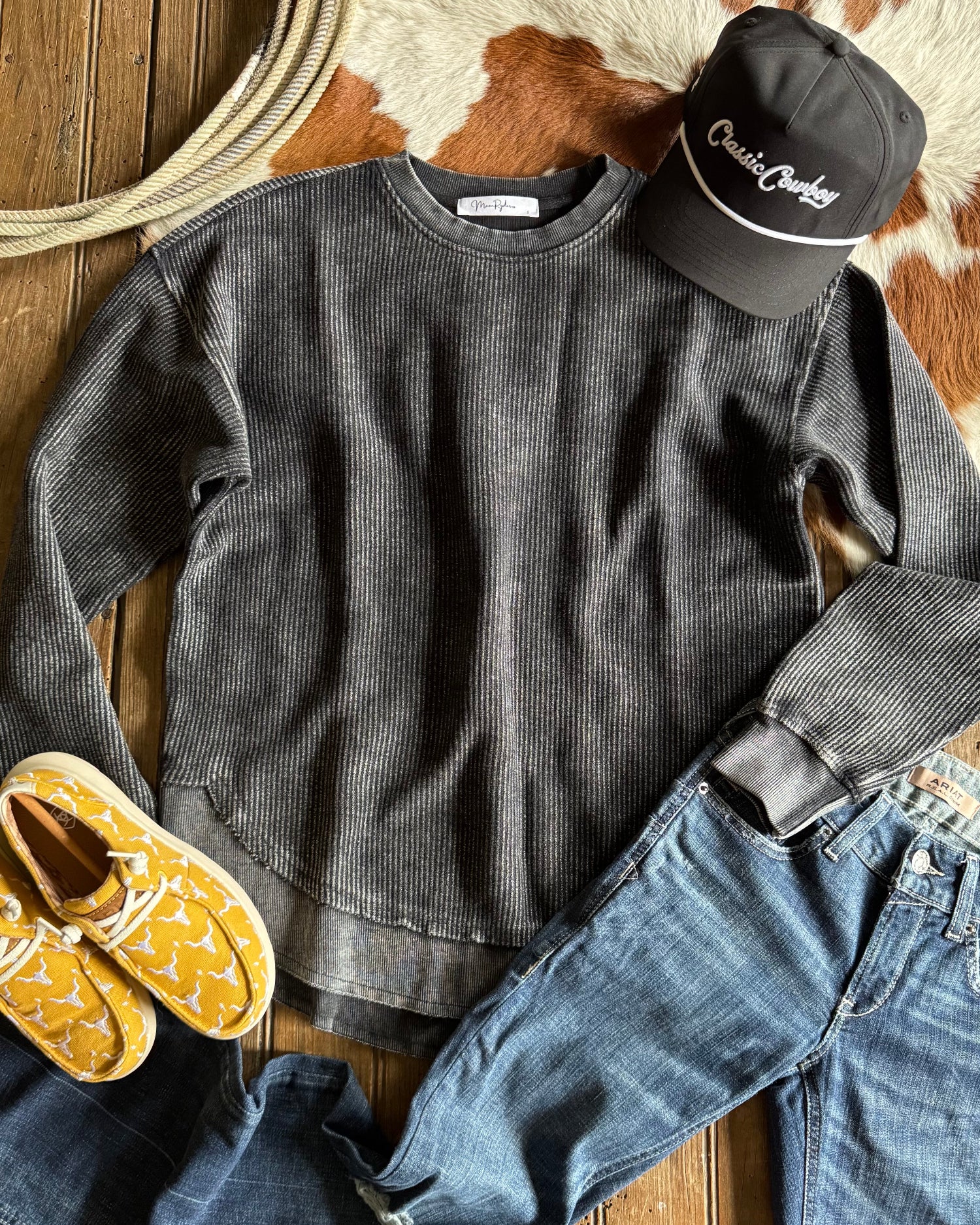 Gray sweatshirt, yellow moccasins, blue jeans, and a black cap on a wooden surface with a cowhide rug.