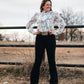 Model standing by a pipe fence in a field, dressed in a stylish modern western outfit.