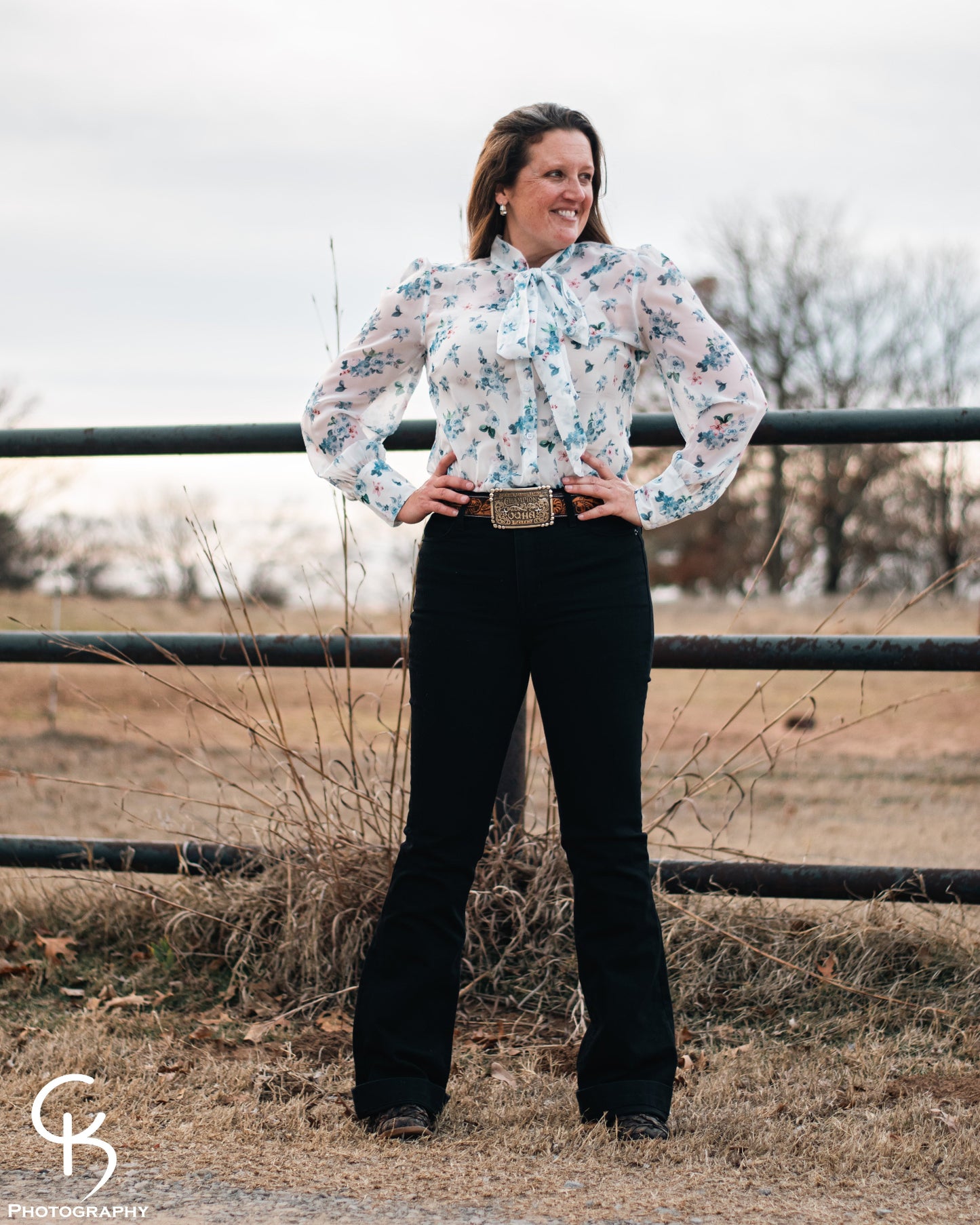 Model standing by a pipe fence in a field, dressed in a stylish modern western outfit.