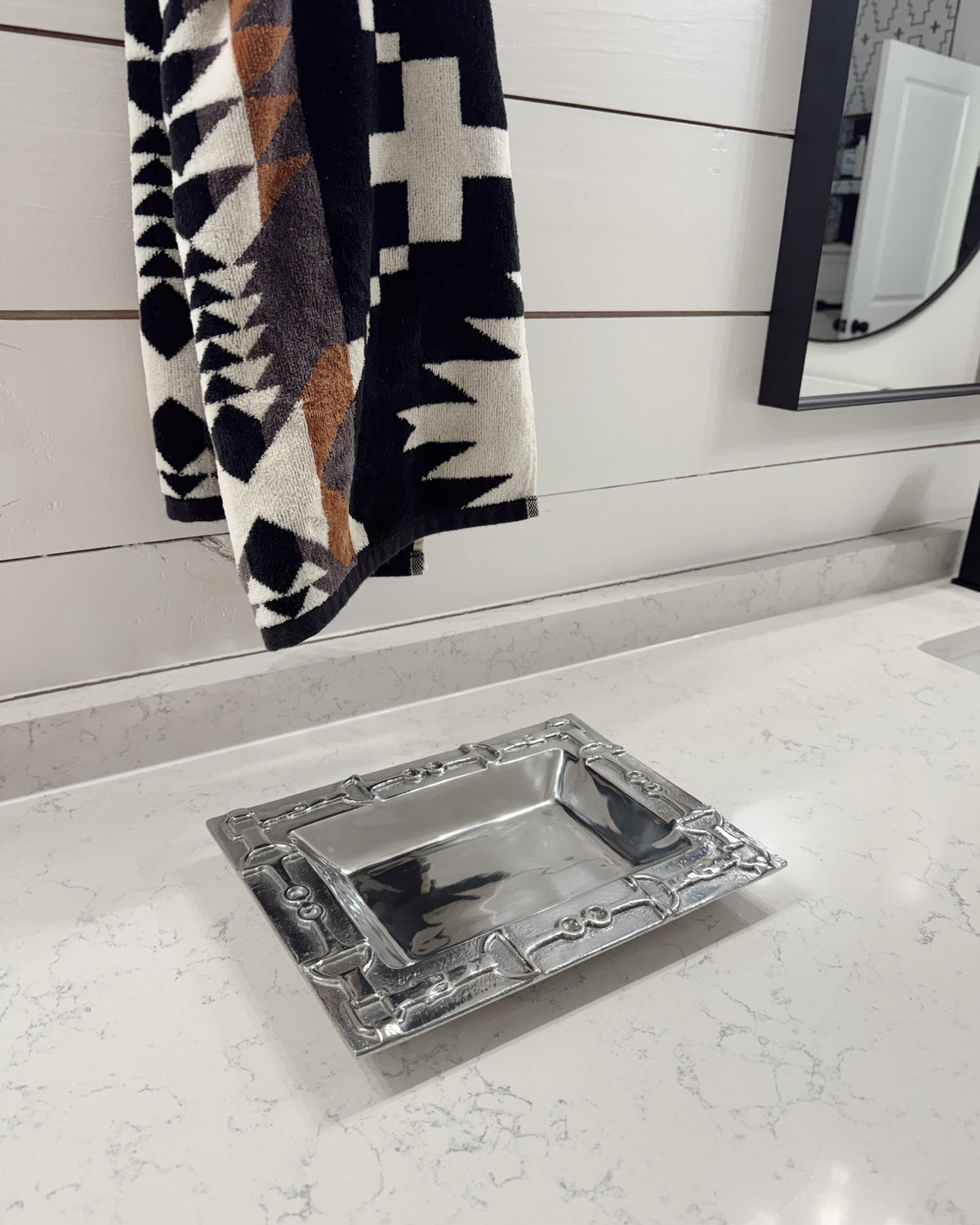 Decorative silver tray on a marble surface with a patterned towel in the background.