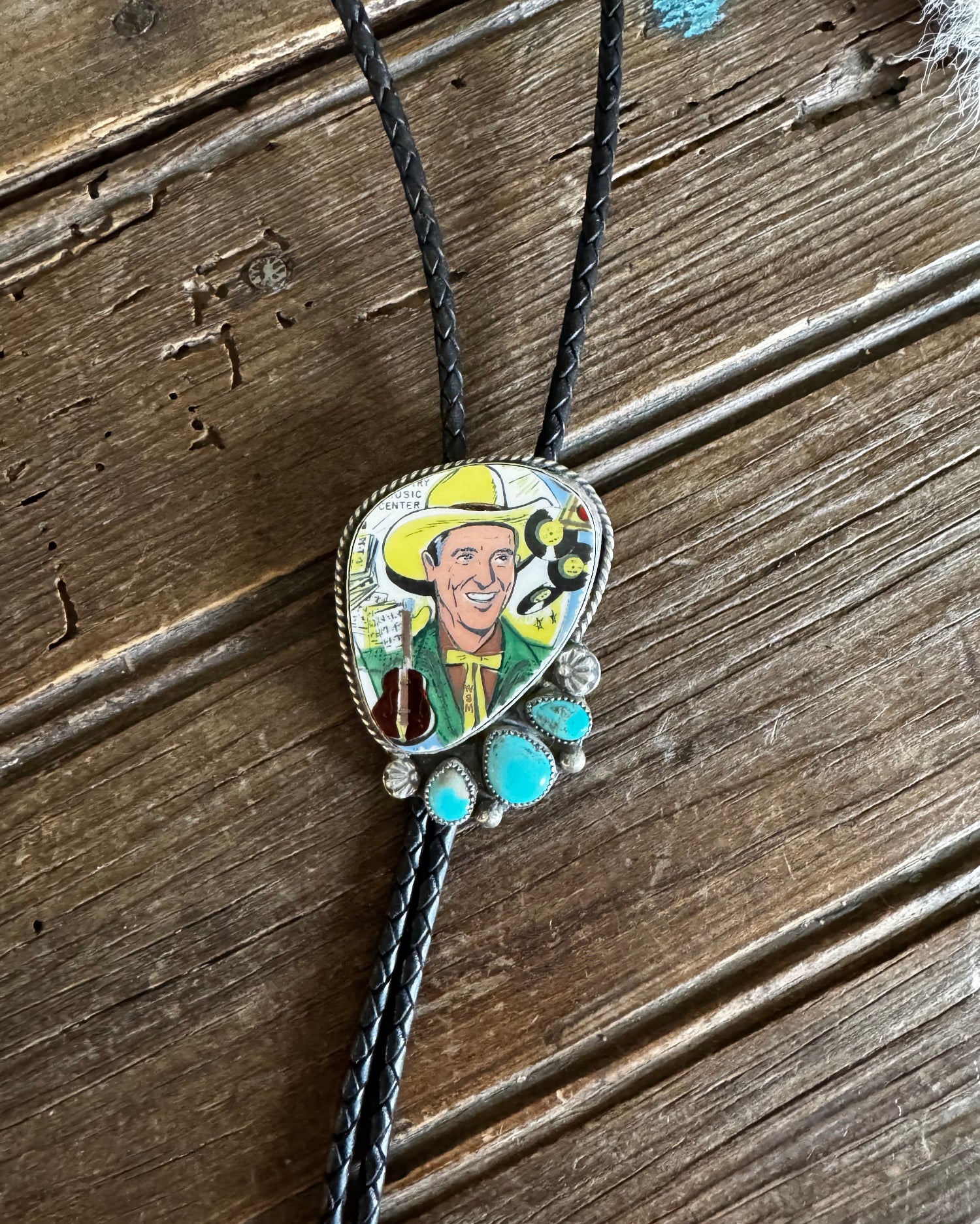 Bolo tie with a colorful pendant featuring a cowboy on a wooden surface