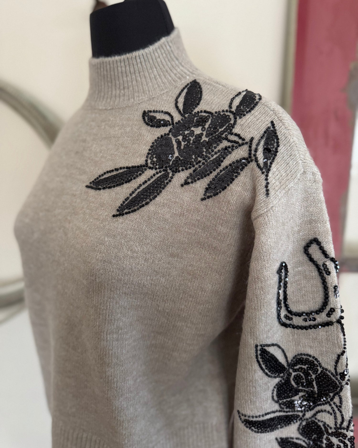 Gray sweater with black floral embroidery on a mannequin against a neutral background